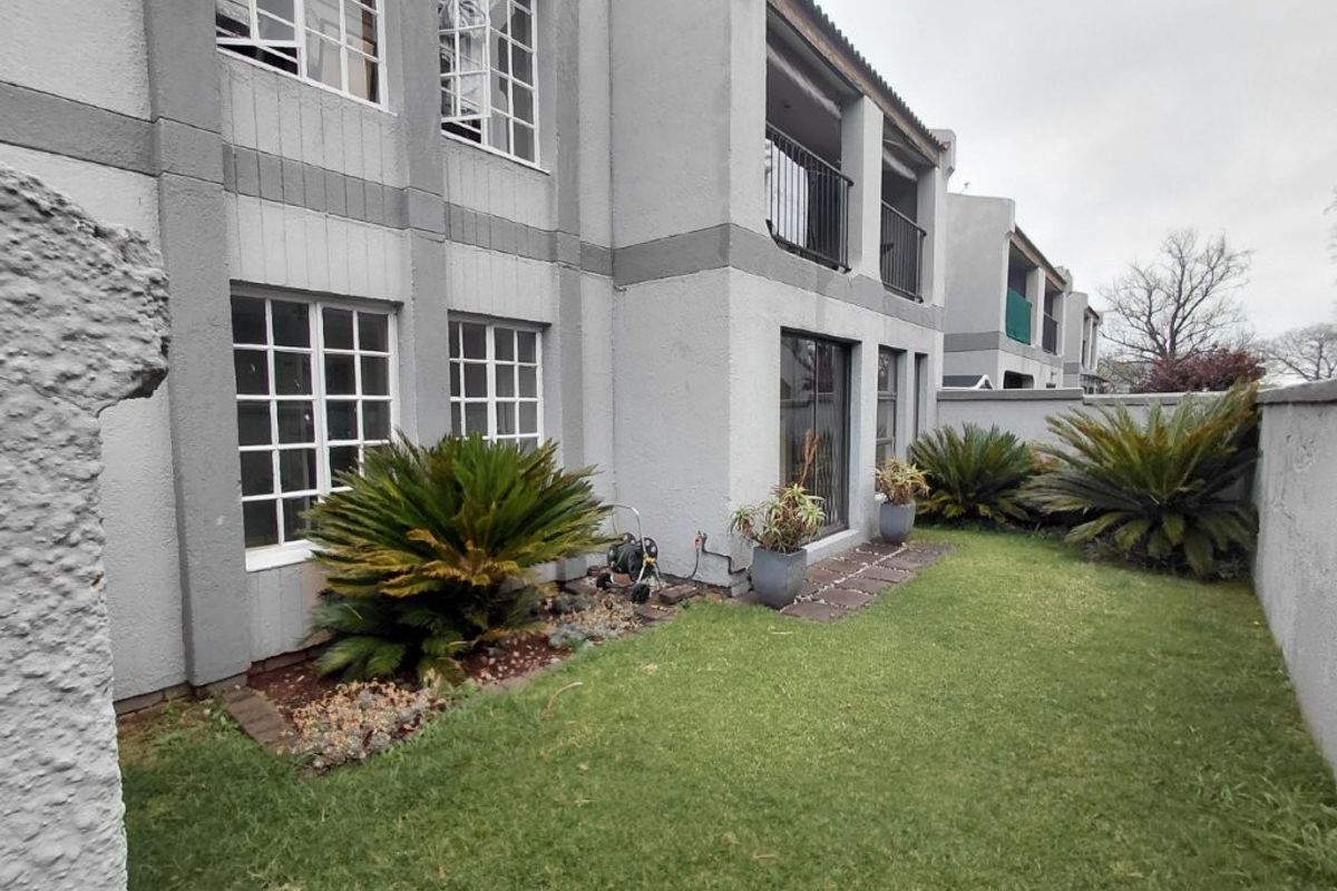 Rear view of the townhouse featuring a private garden, lawn area, sliding glass doors, and an upper-level balcony with metal railings.