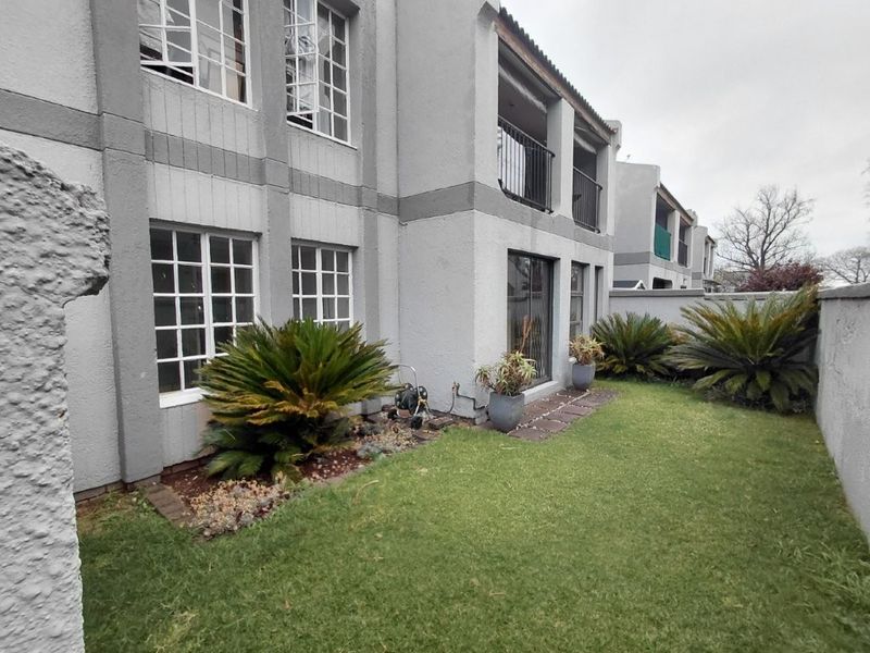 Rear view of the townhouse featuring a private garden, lawn area, sliding glass doors, and an upper-level balcony with metal railings.