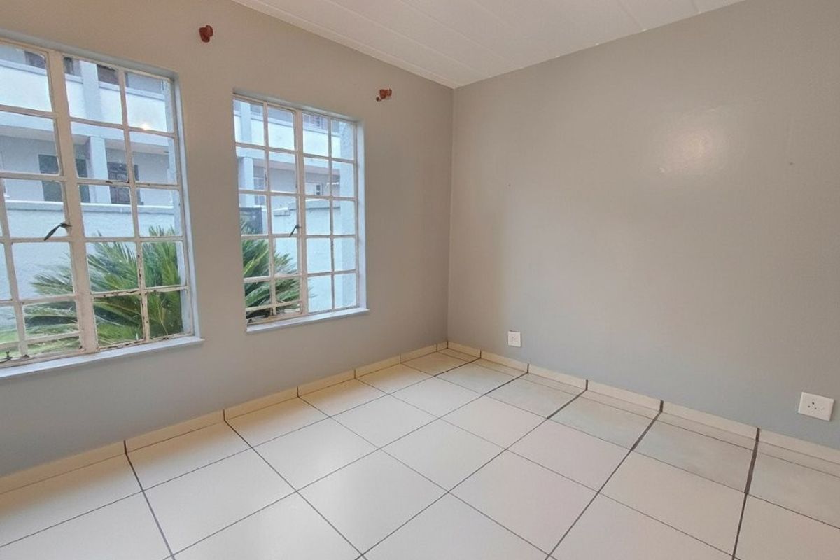 A vacant bedroom featuring neutral wall paint, tiled flooring, and large grid-pattern windows allowing natural light.