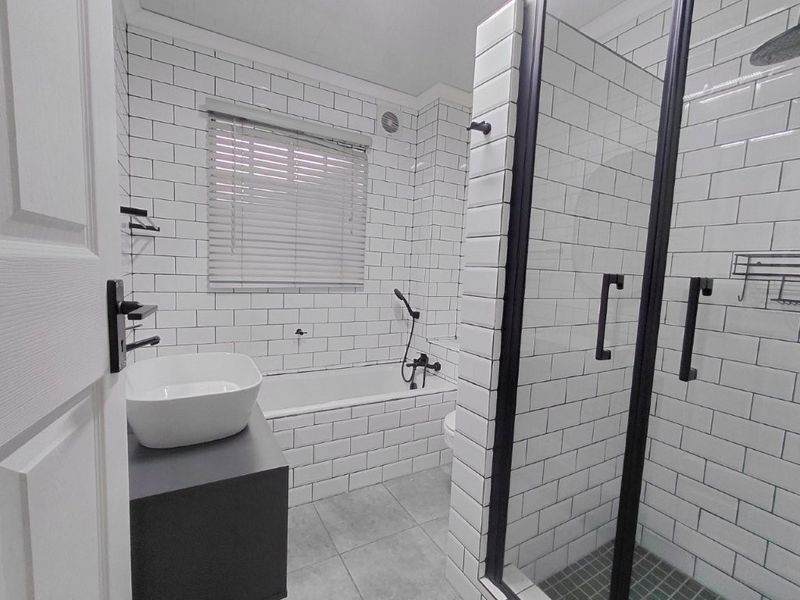 Modern bathroom featuring subway tile walls, a sleek vanity with a vessel basin, a built-in bathtub, and a separate shower enclosure with black fixtures.
