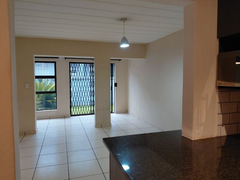 Open plan living area featuring tiled flooring, granite kitchen countertops, and direct access to the exterior through a security gate.