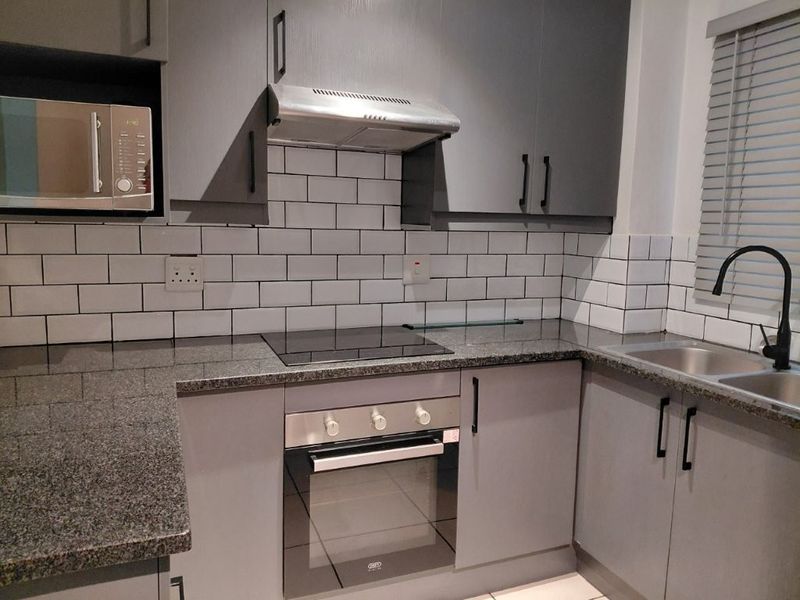Modern kitchen featuring grey cabinetry, granite countertops, subway tile backsplash, and integrated appliances including an oven, hob, and extractor fan.