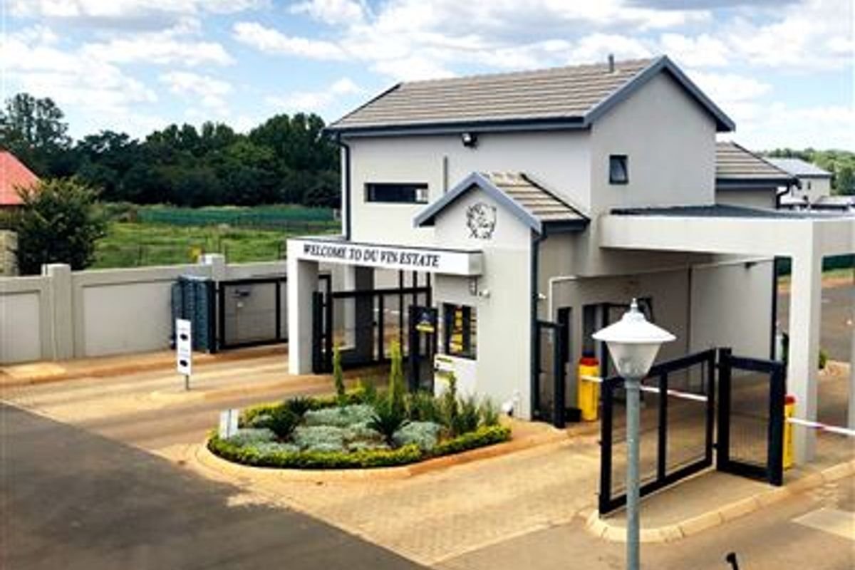 The secure entrance gatehouse of Du Vin Estate, featuring a paved driveway, landscaped garden bed, and automated access control infrastructure.