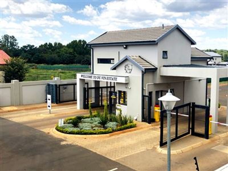 The secure entrance gatehouse of Du Vin Estate, featuring a paved driveway, landscaped garden bed, and automated access control infrastructure.