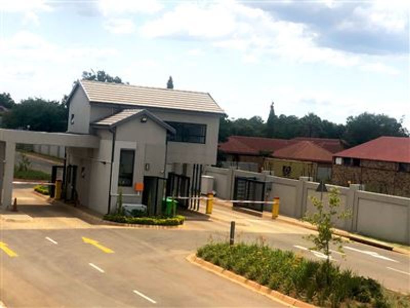 A view of the secure gated entrance and guardhouse for the residential estate, featuring paved access roads and perimeter walling.