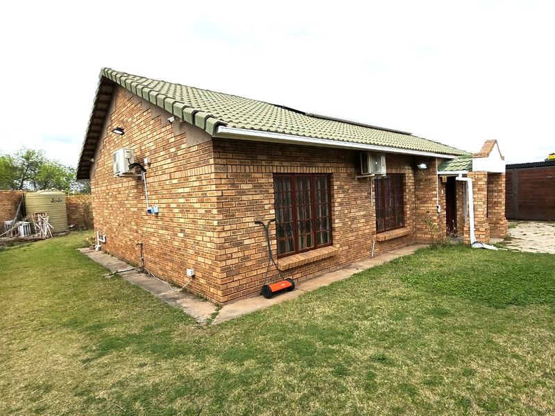 Rear view of a face brick townhouse featuring a tiled roof, air conditioning units, and a private garden area with a water storage tank.