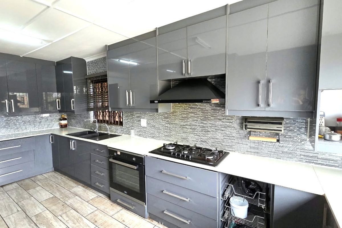 Modern kitchen featuring sleek grey cabinetry, stone countertops, a gas hob with extractor fan, and a stylish mosaic tile backsplash.