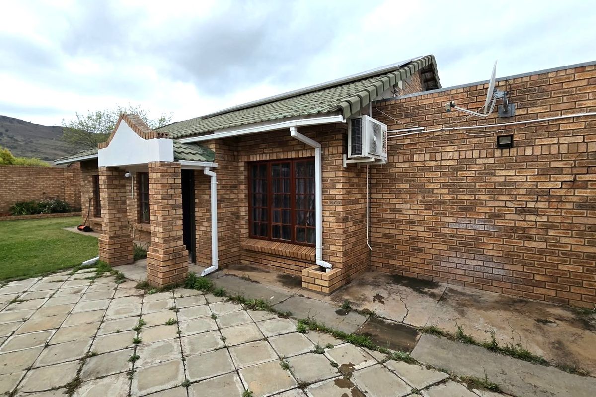 Rear view of a face brick townhouse featuring a paved patio area, external air conditioning unit, and surrounding boundary wall.