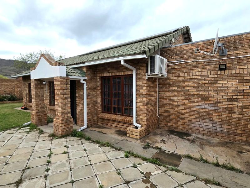 Rear view of a face brick townhouse featuring a paved patio area, external air conditioning unit, and surrounding boundary wall.