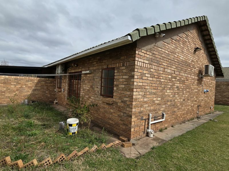 Rear view of a face brick townhouse featuring a tiled roof, external air conditioning unit, and a private garden area with boundary walling.
