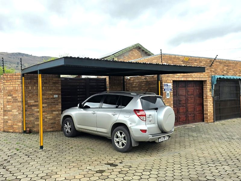 Front exterior view of the townhouse featuring a paved driveway, a covered carport, and a brick facade with a secure garage entrance.