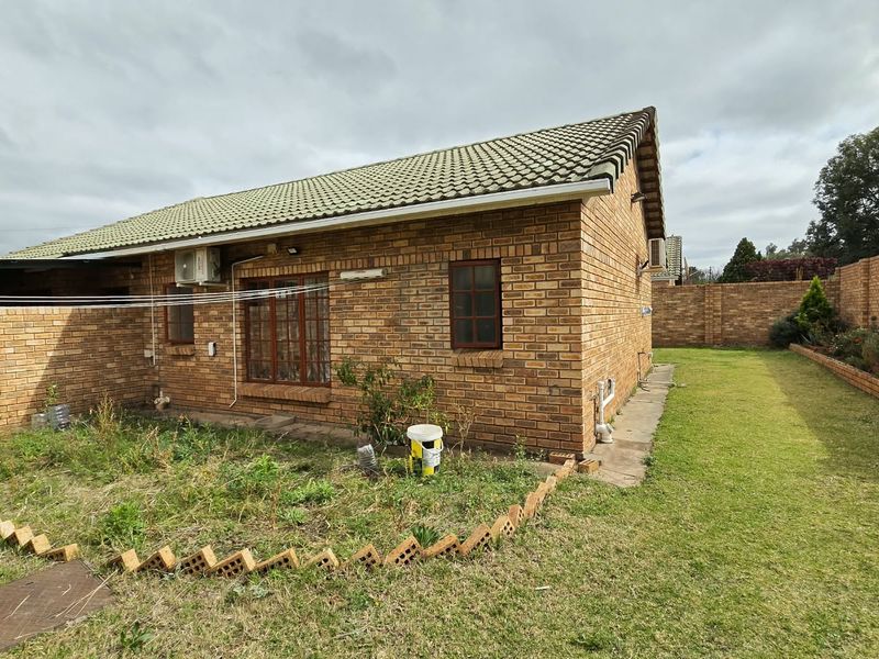 Rear view of a face brick townhouse featuring a tiled roof, air conditioning unit, and a private garden area with perimeter walling.
