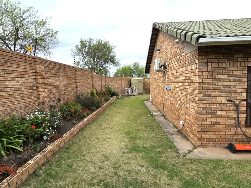 A side view of the townhouse featuring a face brick exterior, a well-maintained garden bed, and a secure boundary wall.
