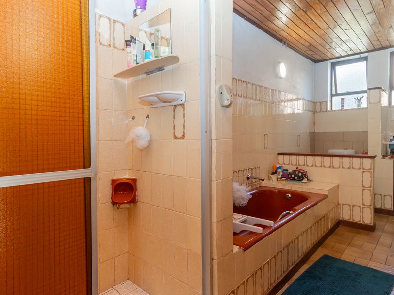 A dated bathroom featuring a built-in bathtub, separate shower enclosure, tiled finishes, and a timber ceiling, offering potential for modern renovation.