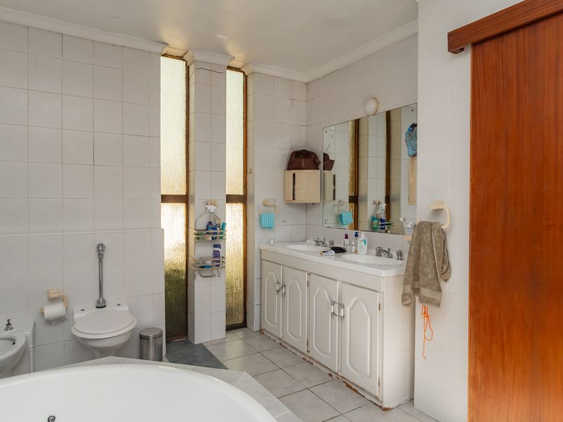 A spacious bathroom featuring a double vanity, built-in bathtub, bidet, and toilet, finished with floor-to-ceiling wall tiles and vertical windows for natural light.