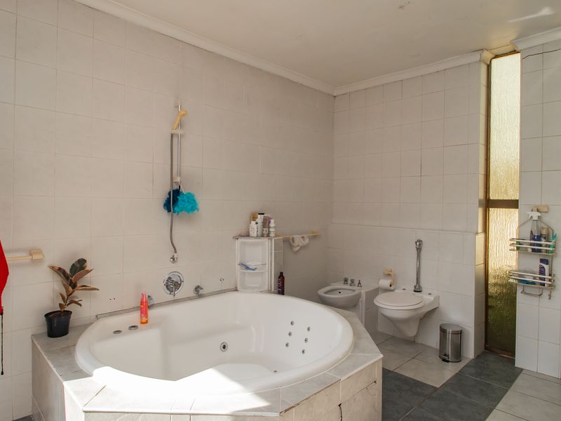Spacious bathroom featuring a built-in corner spa bath, wall-mounted toilet, bidet, and floor-to-ceiling tiled finishes with natural light from frosted glass windows.