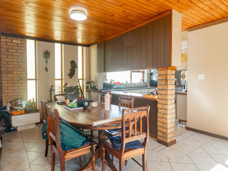 Open plan dining and kitchen area featuring a timber ceiling, brick accents, and tiled flooring, offering a functional layout with a breakfast bar.