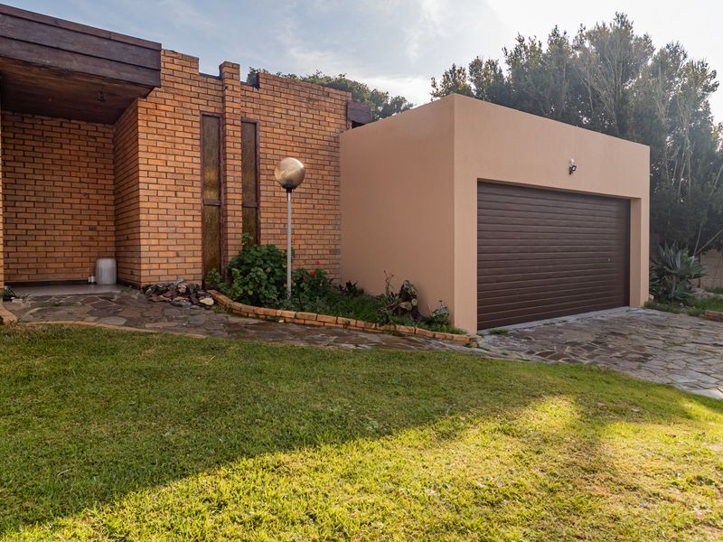 Front exterior view of the house featuring a brick facade, a single garage with a brown door, and a stone-paved driveway and walkway.