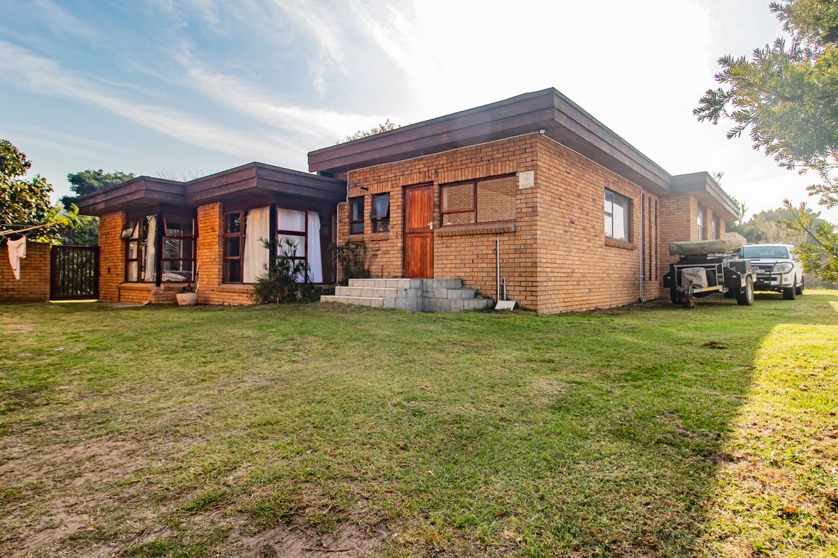 Rear view of a single-story face brick house featuring a flat roof design, timber entrance door, and concrete steps leading to the garden.
