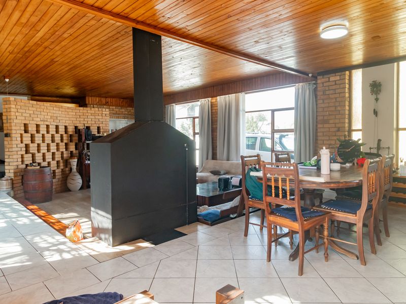 Spacious open-plan living and dining area featuring a prominent central metal fireplace, exposed brick walls, and a warm timber-clad ceiling.