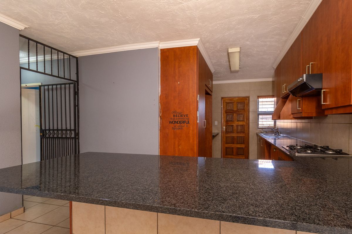 A functional kitchen featuring granite countertops, built-in wooden cabinetry, a gas hob with extractor, and a tiled backsplash, offering a practical layout.