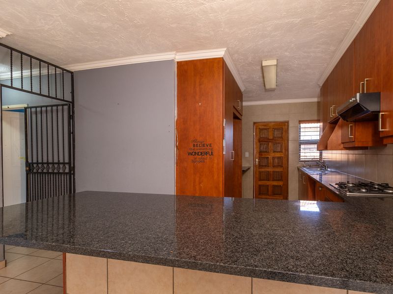 A functional kitchen featuring granite countertops, built-in wooden cabinetry, a gas hob with extractor, and a tiled backsplash, offering a practical layout.