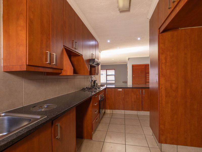 A functional kitchen featuring warm-toned wooden cabinetry, dark granite countertops, a gas hob, and tiled flooring, offering a clean and practical workspace.