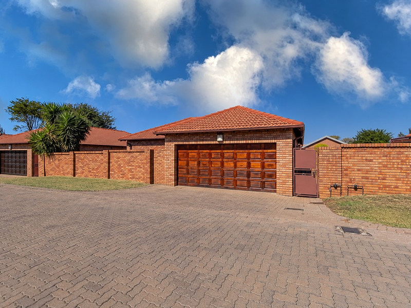 Front exterior view of the townhouse featuring a brick facade, tiled roof, paved driveway, and a secure wooden garage door.