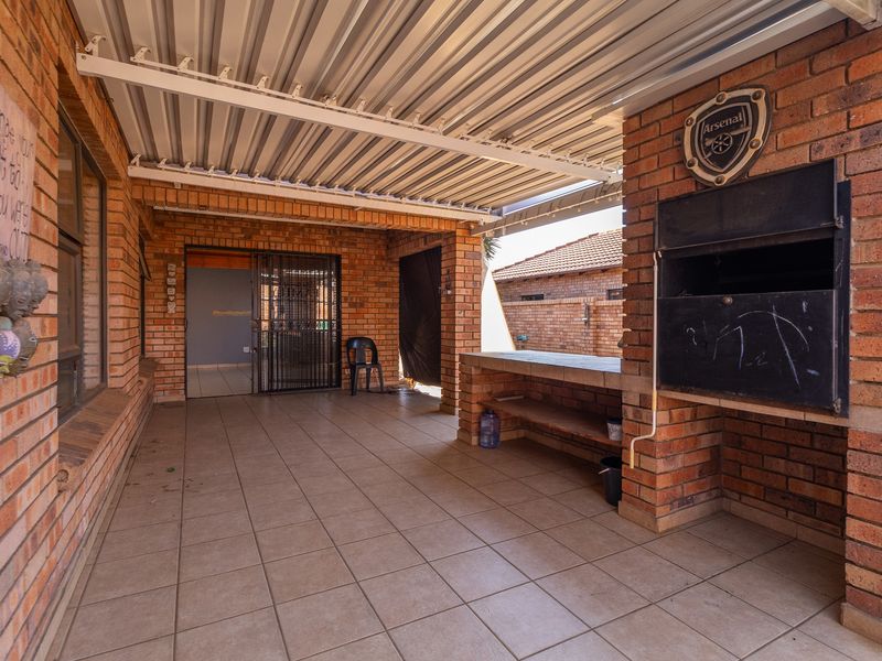 Covered patio area featuring exposed brick walls, tiled flooring, and a built-in braai, providing a functional outdoor entertainment space.