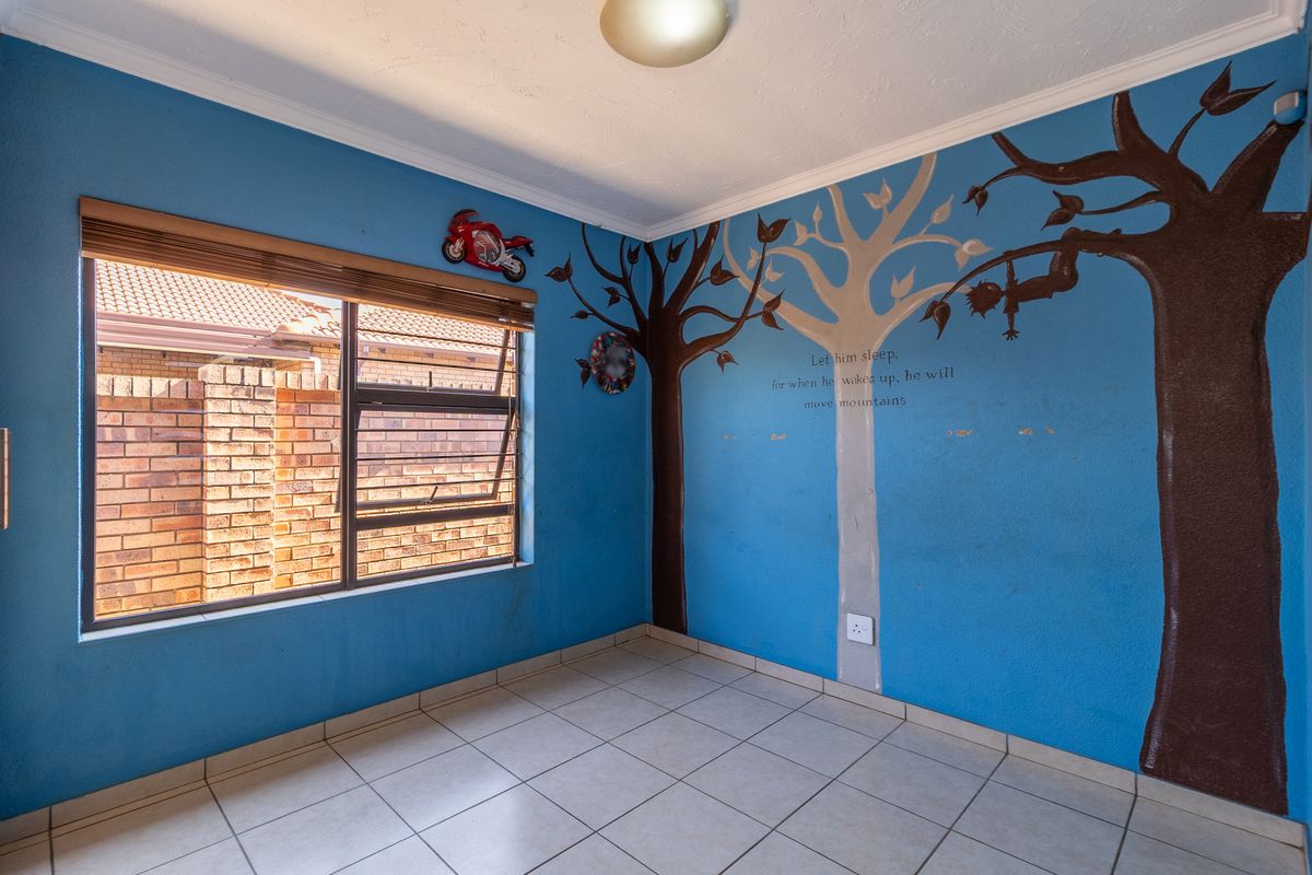 An empty bedroom featuring tiled flooring, an aluminium window with blinds, and blue painted walls with a decorative mural.