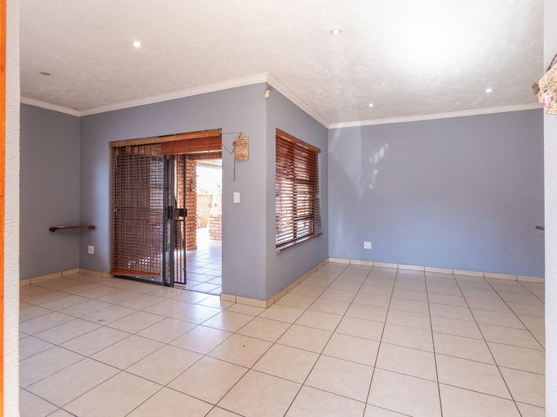 An empty, open-plan living area featuring neutral tiled flooring, recessed downlighting, and a sliding glass door providing access to an outdoor patio space.