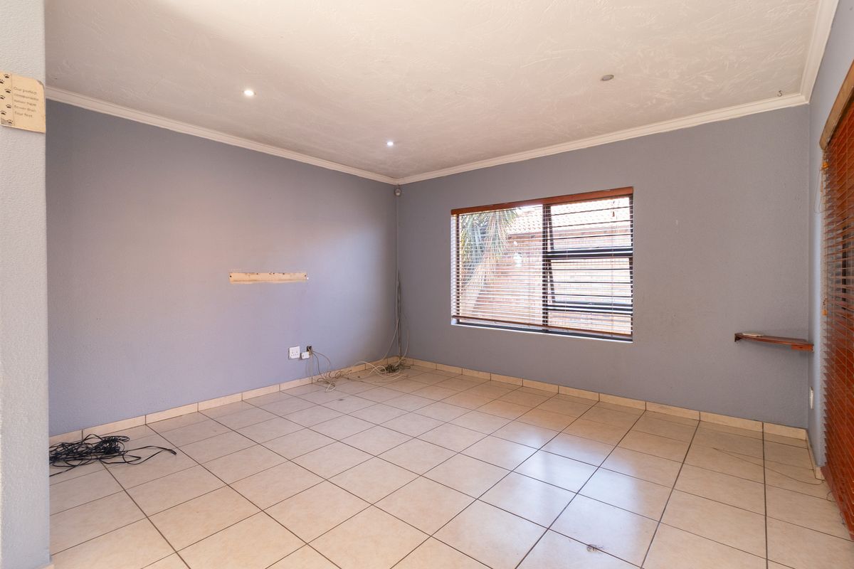 An empty living room featuring tiled flooring, recessed downlights, and venetian blinds, providing a blank canvas for interior design.