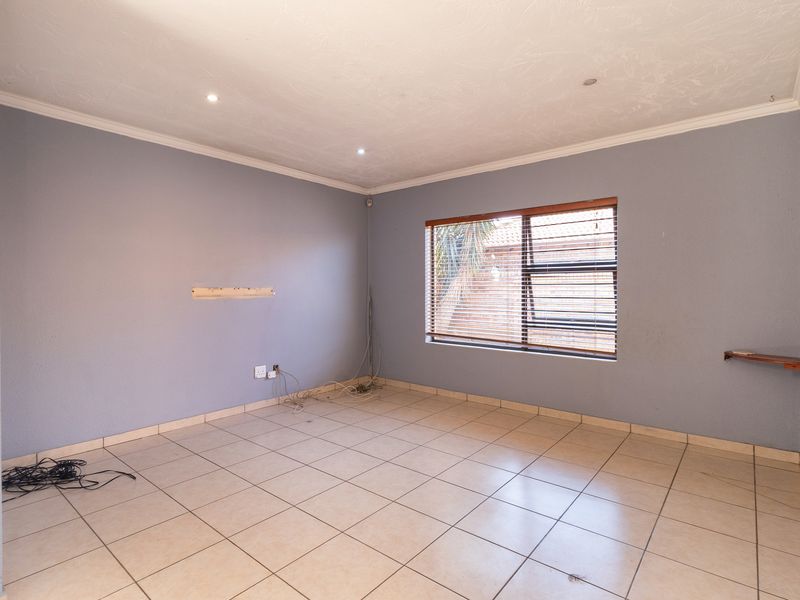 An empty living room featuring tiled flooring, recessed downlights, and venetian blinds, providing a blank canvas for interior design.