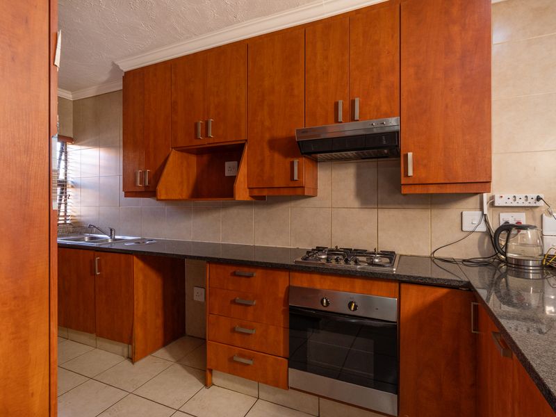 Functional kitchen featuring warm-toned wooden cabinetry, granite countertops, a gas hob, built-in oven, and tiled backsplash with neutral floor tiles.