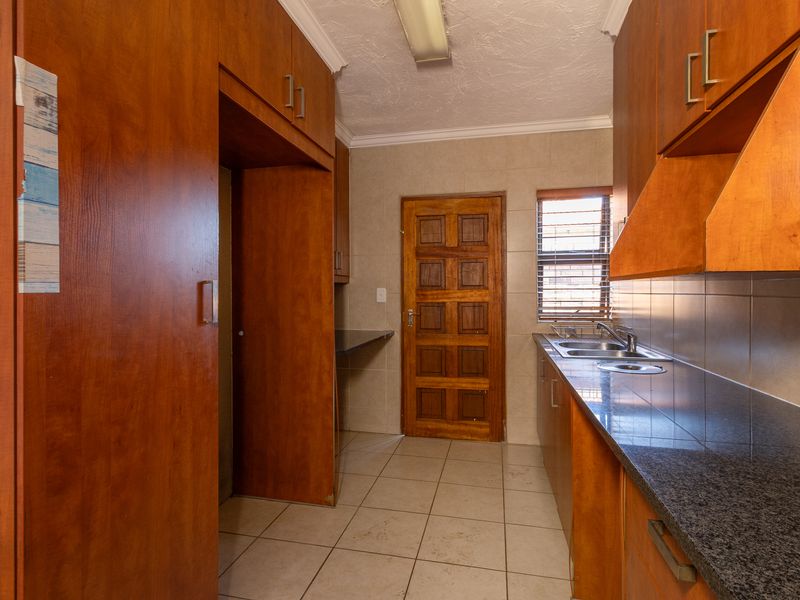 A functional kitchen featuring built-in wooden cabinetry, granite countertops, a stainless steel sink, and tiled flooring with a rear access door.