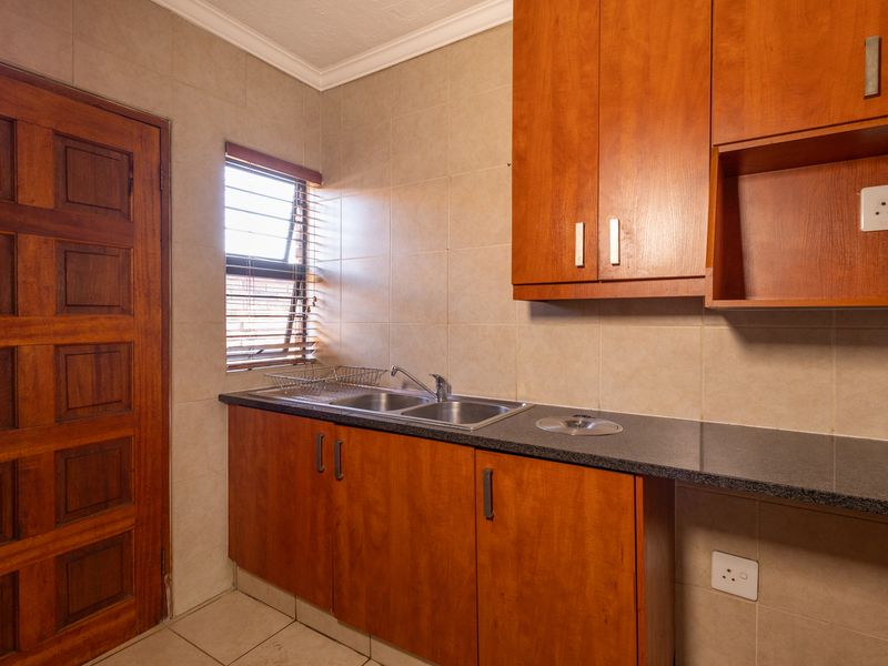 A functional scullery area featuring wooden cabinetry, granite countertops, a double stainless steel sink, and tiled wall finishes.