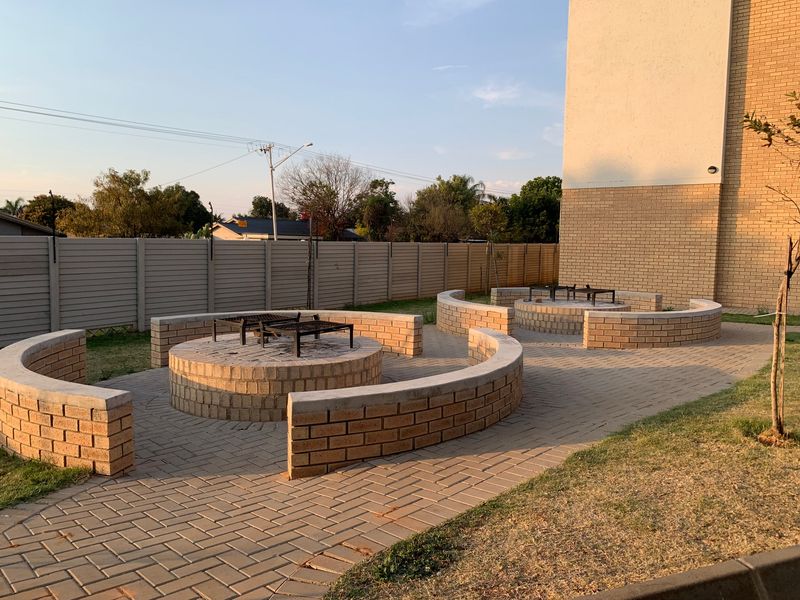 Communal outdoor entertainment area featuring paved flooring, built-in brick braai pits, and curved brick seating walls.