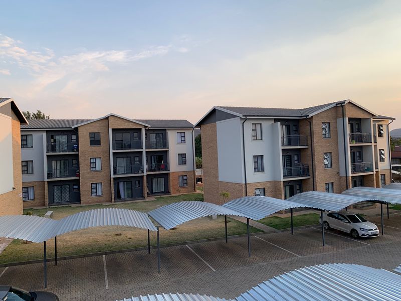 Exterior view of a modern apartment complex featuring brick facades, private balconies, and covered carport parking bays.
