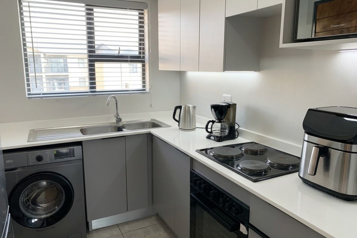 Modern kitchen featuring grey cabinetry, white countertops, integrated electric hob and oven, stainless steel sink, and tiled flooring with under-cabinet lighting.