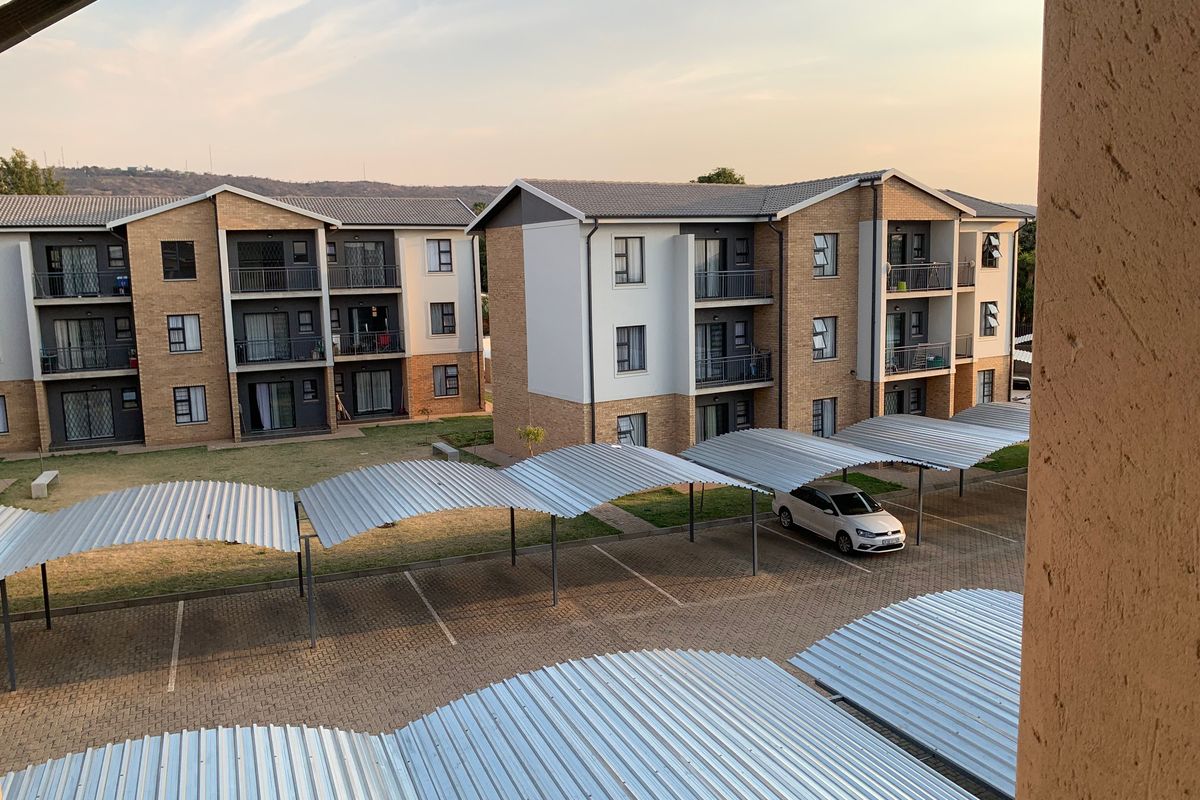 Elevated view of an apartment complex featuring brick facades, tiled roofs, and covered parking bays within a paved residential courtyard.