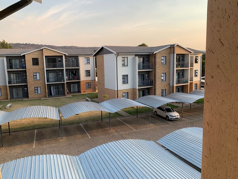Elevated view of an apartment complex featuring brick facades, tiled roofs, and covered parking bays within a paved residential courtyard.