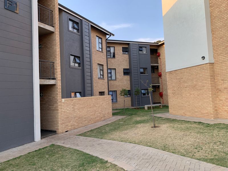 Exterior view of a modern apartment complex featuring face brick facades, paved walkways, and communal garden areas.