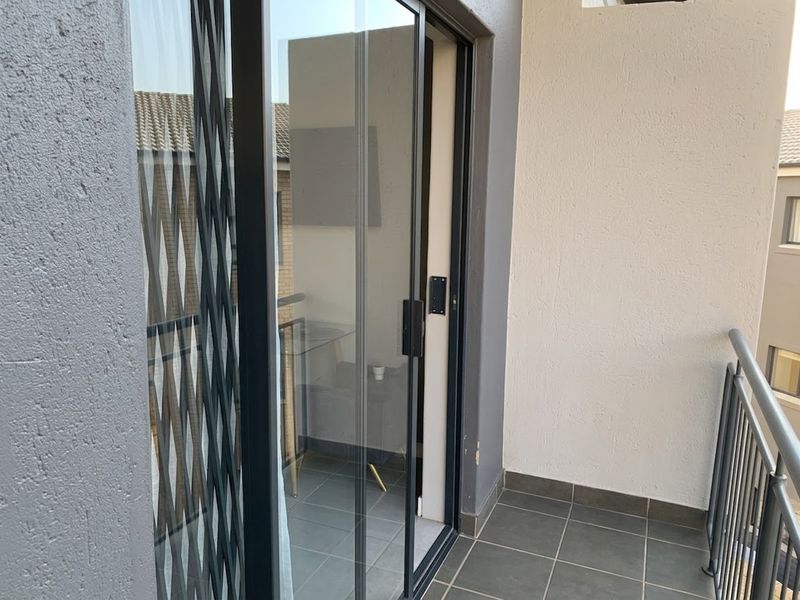 A compact balcony featuring tiled flooring, a metal safety railing, and a sliding glass door with an integrated security gate.