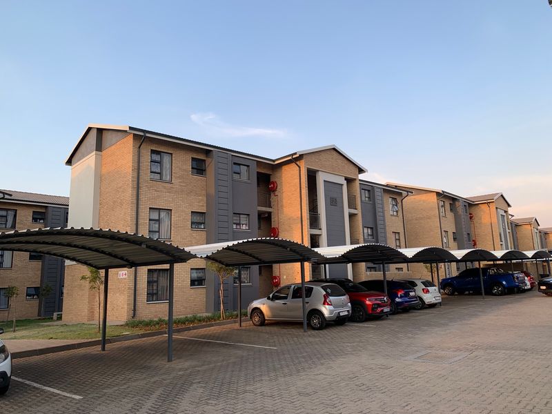 Exterior view of a modern multi-story apartment complex featuring brick facades, covered parking bays, and paved driveway areas.