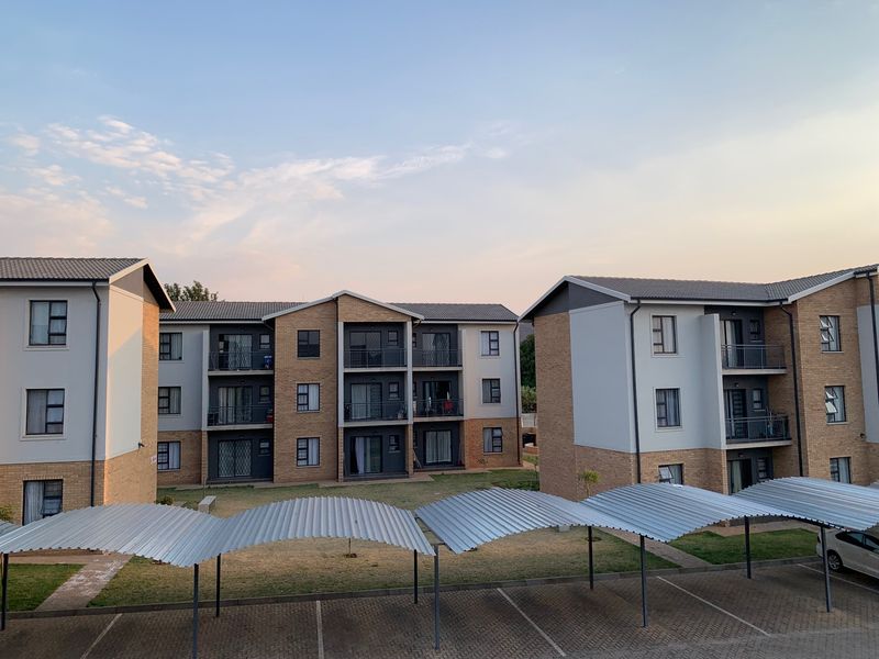Exterior view of a modern apartment complex featuring brick and plaster facades, private balconies, and a covered carport parking area.