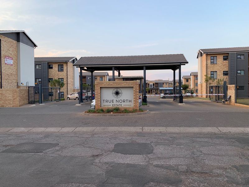 The main entrance to True North Estate, featuring a secure boom gate, brick facade buildings, and paved driveway access.