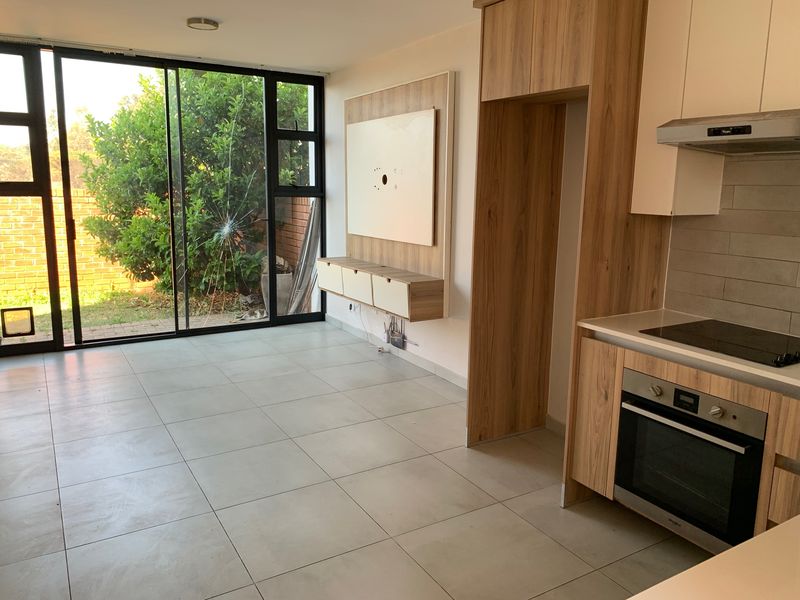 Open-plan living and kitchen area featuring modern cabinetry, built-in appliances, tiled flooring, and large sliding doors leading to the garden.