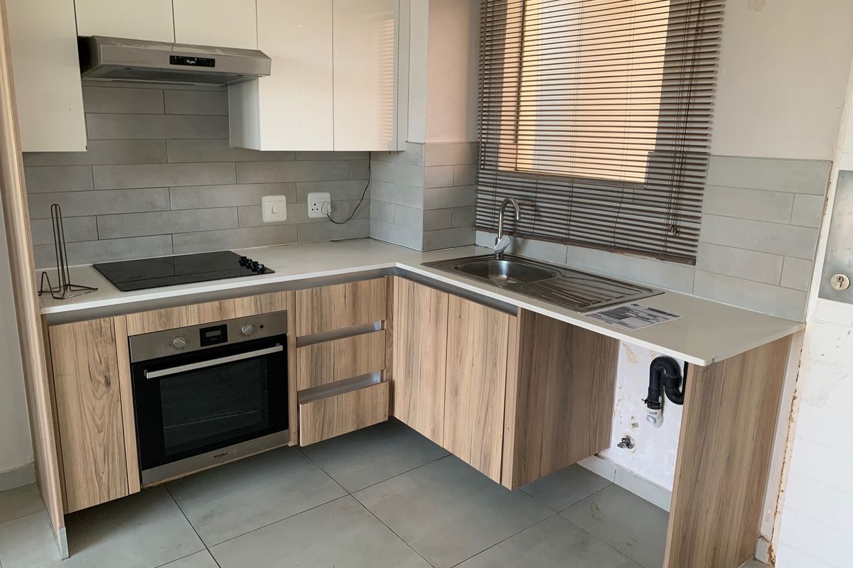 Modern kitchen featuring wood-look cabinetry, stone countertops, built-in oven, and hob. Requires minor finishing work to the cabinetry and wall area under the sink.