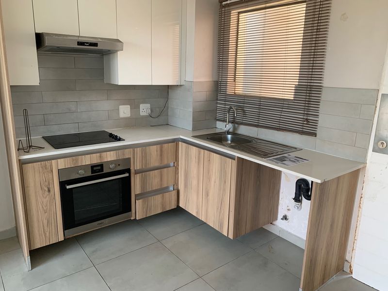 Modern kitchen featuring wood-look cabinetry, stone countertops, built-in oven, and hob. Requires minor finishing work to the cabinetry and wall area under the sink.