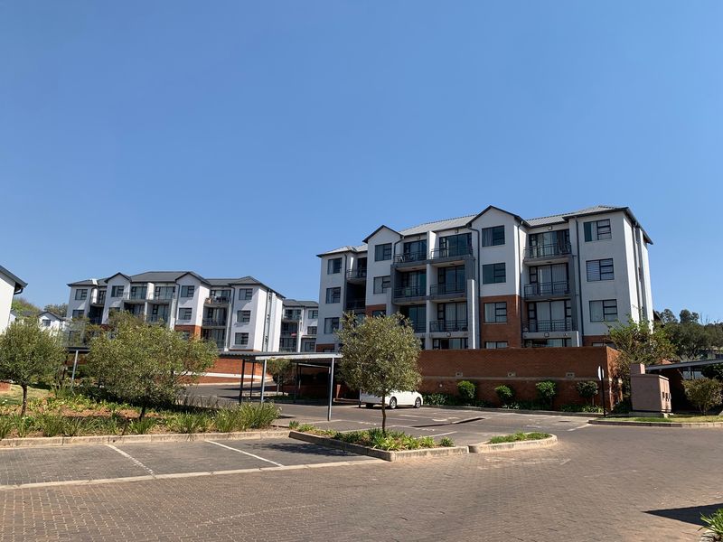 Exterior view of multi-story apartment complex featuring paved parking areas, covered parking bays, and residential balconies.